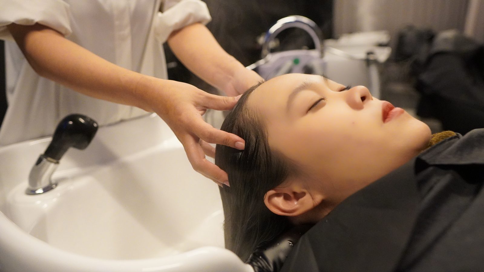 A therapist gently massaging a guest's scalp at the shampoo bowl